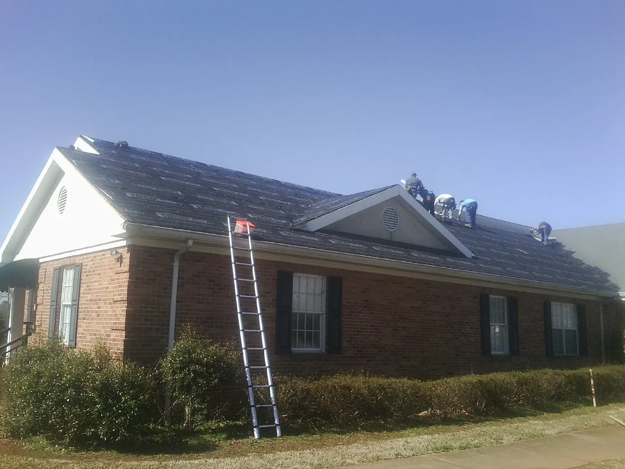 Crew tearing shingles off a brick ranch roof with a ladder set — Metal Roof Repair work by our crew in Harrington