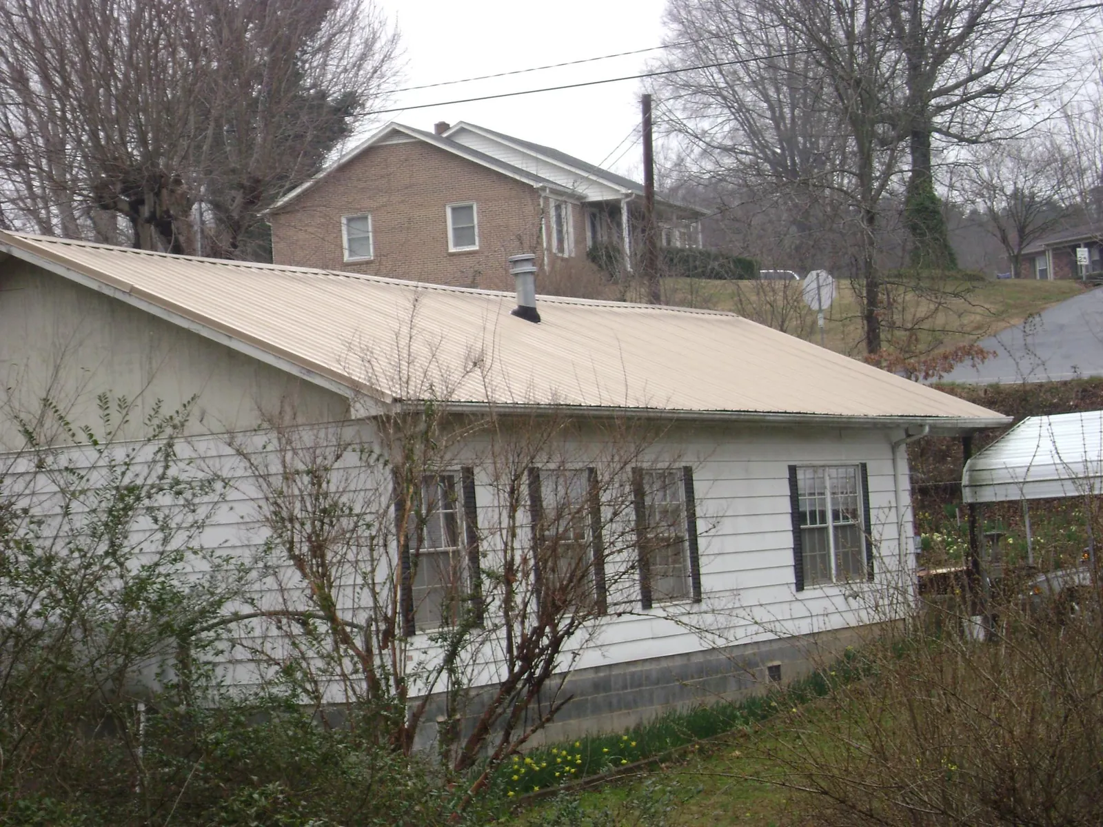 Tan metal roof on a white sided house set into a hillside — Commercial Roofing by Roofing Brothers in Harrington